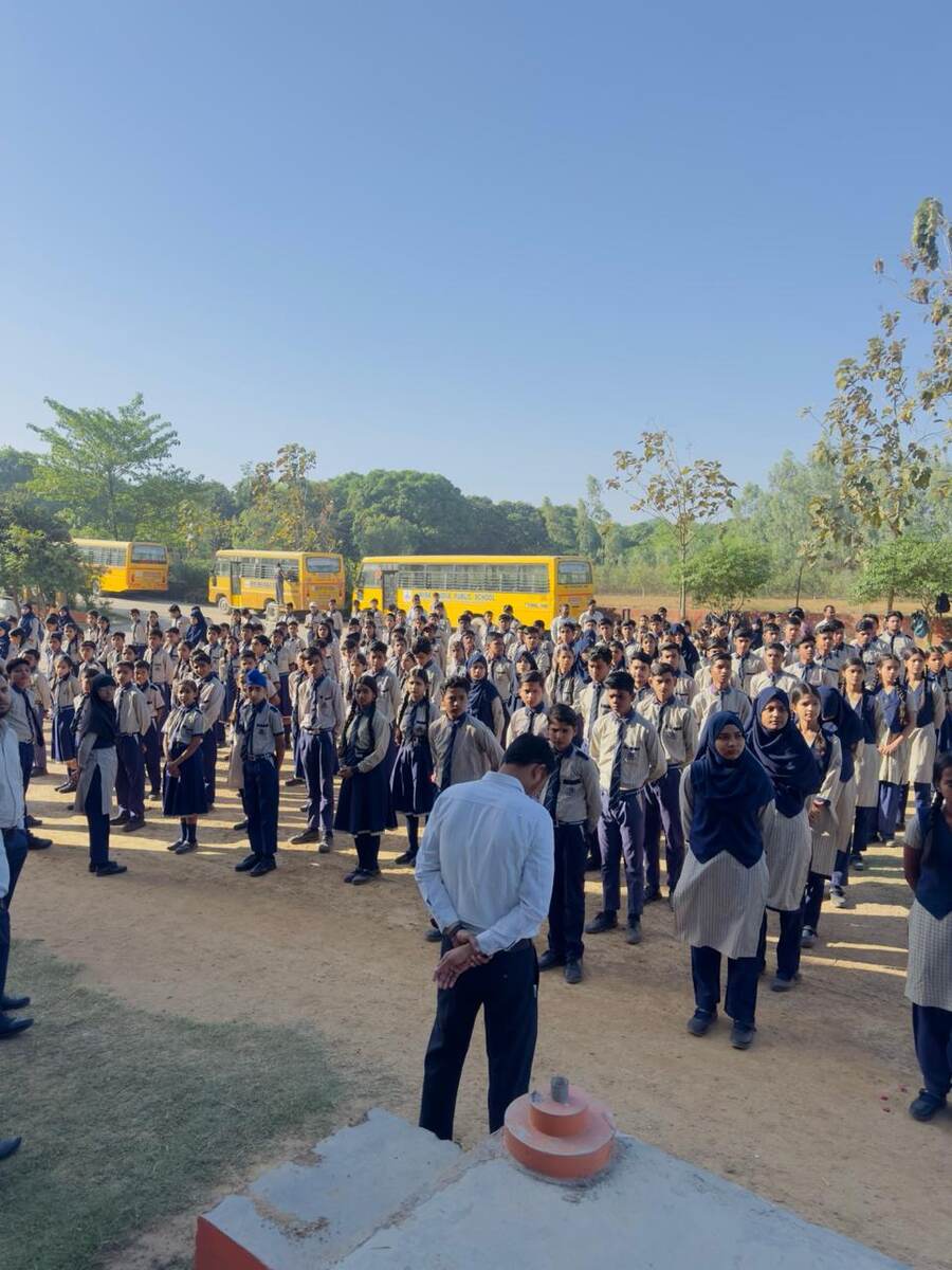 Senior wing students standing in assembly formation with school buses parked behind them